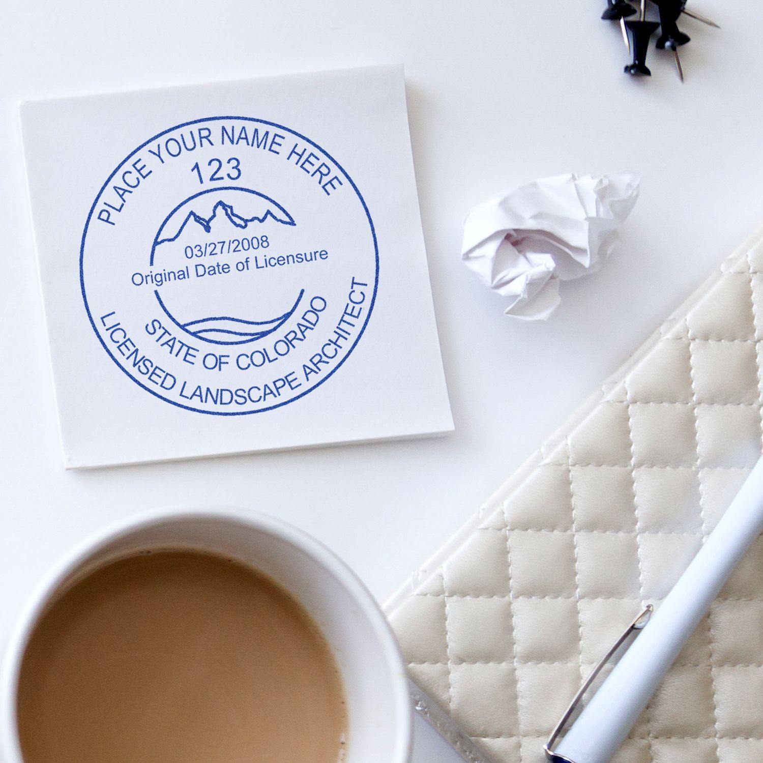 Xstamper Landscape Architect Pre-Inked Rubber Stamp of Seal on paper with coffee cup, pen, and crumpled paper on a white desk.