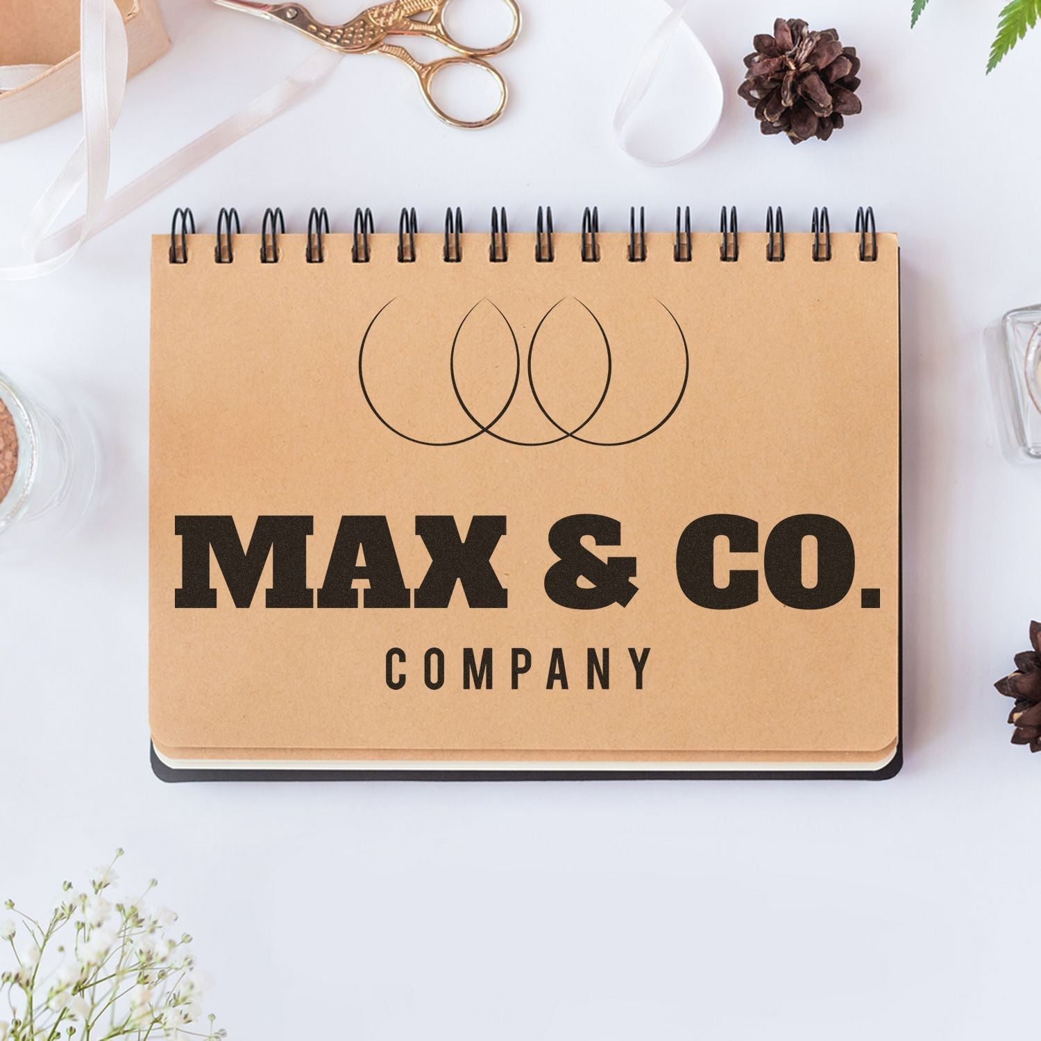 A Custom Rubber Stamp Size 8 x 10 is used to stamp MAX & CO. COMPANY on a spiral notebook, surrounded by office supplies.