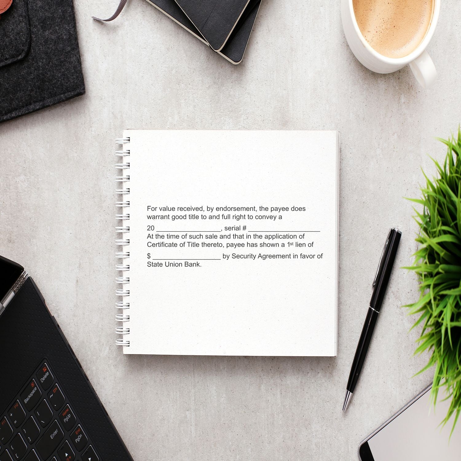 A desk with a notebook stamped using the 11 Line Custom Rubber Stamp with Wood Handle, surrounded by a laptop, pen, coffee, and plant.