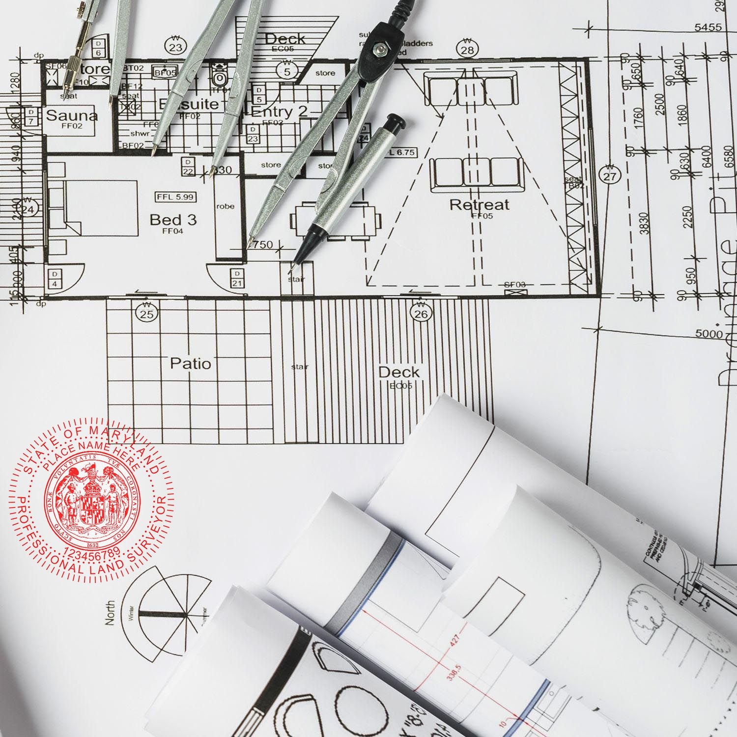 Self Inking Maryland Land Surveyor Stamp on architectural blueprints with drafting tools and rolled plans in the background.