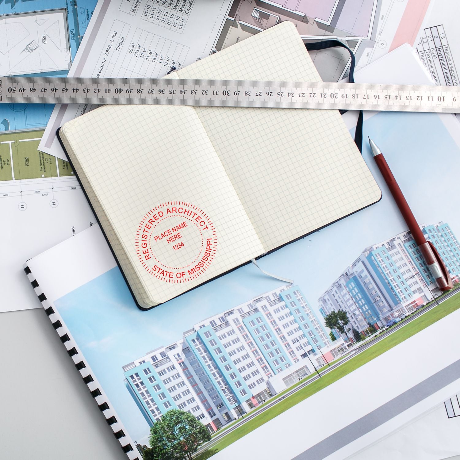 Self Inking Mississippi Architect Stamp in use on an open notebook, surrounded by architectural plans, a ruler, and a pencil.