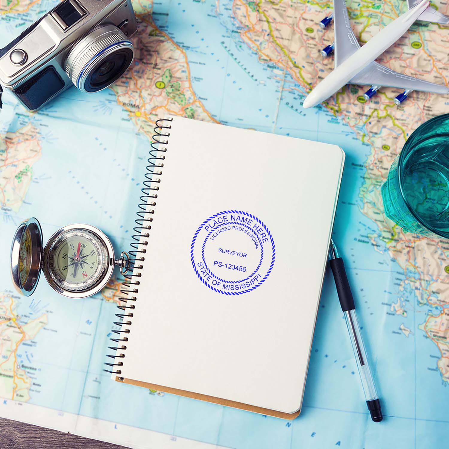 Self Inking Mississippi Land Surveyor Stamp on a notebook, surrounded by a compass, pen, camera, and a map.