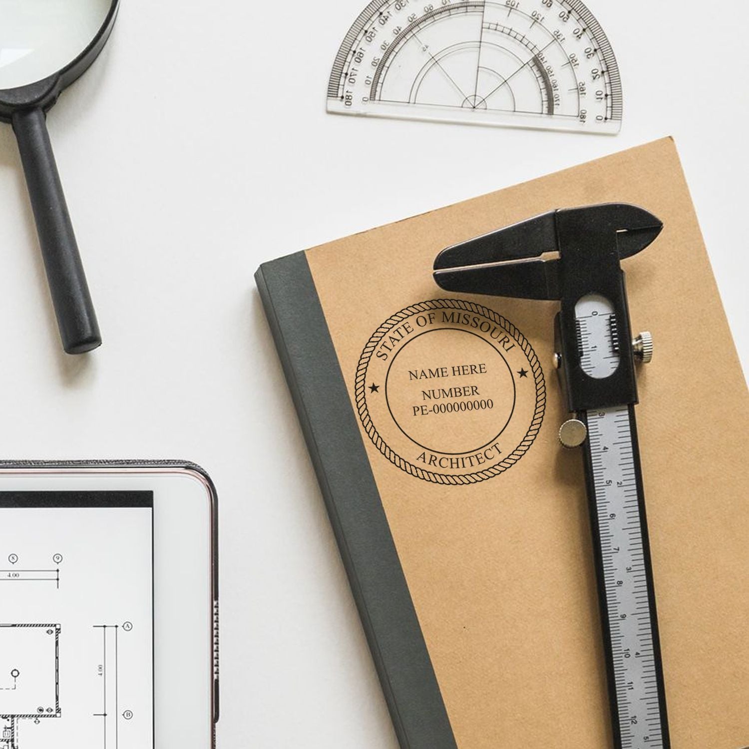 Self Inking Missouri Architect Stamp on a notebook with a caliper, protractor, magnifying glass, and tablet with architectural plans.