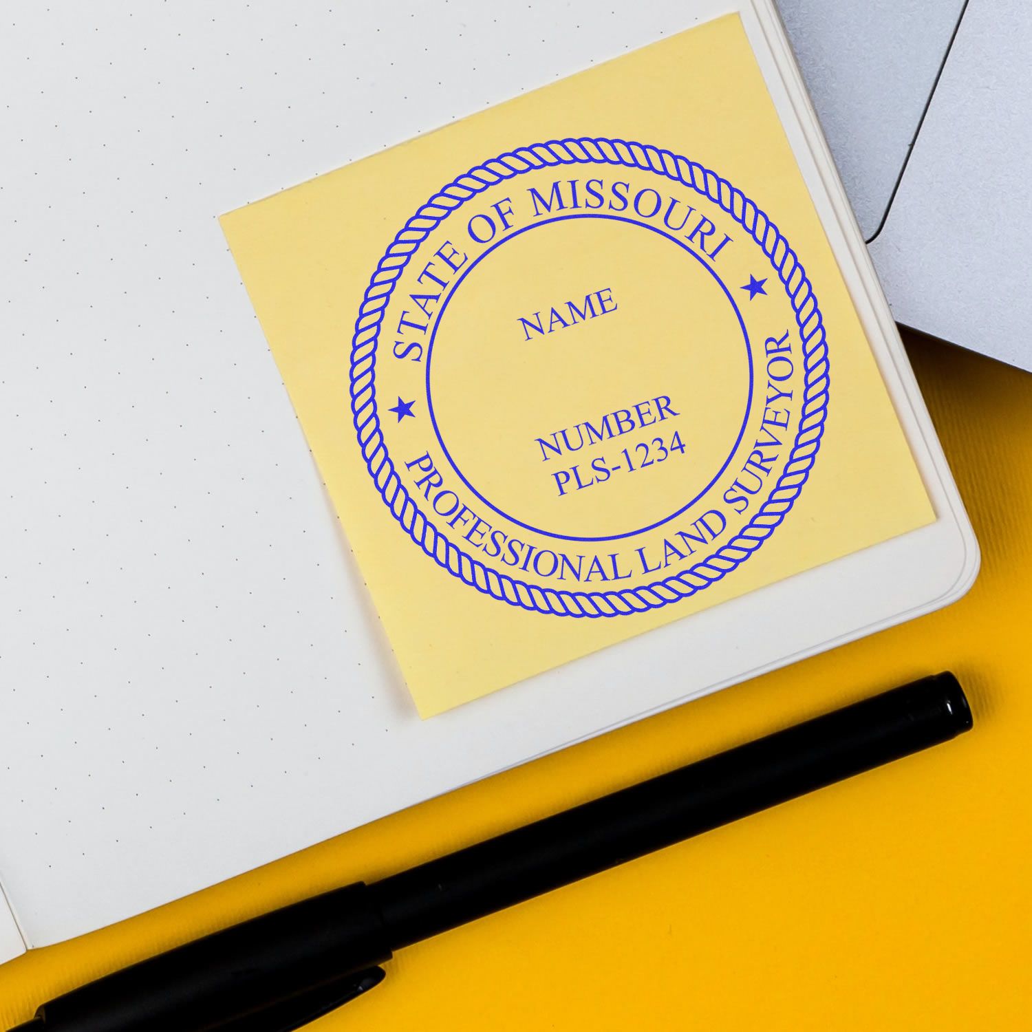 Self Inking Missouri Land Surveyor Stamp on yellow paper, next to a black pen and a notebook.