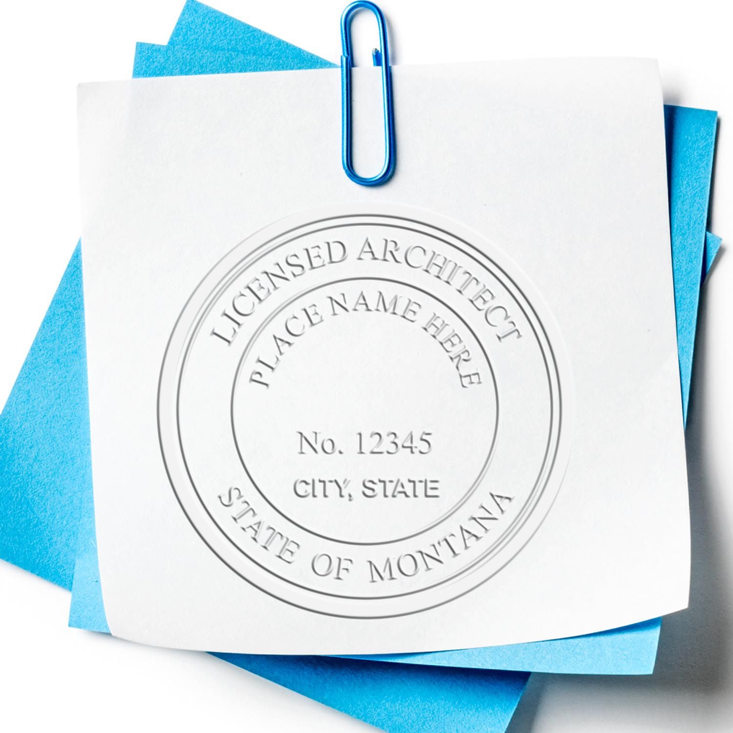 A lifestyle photo showing a stamped image of the Handheld Montana Architect Seal Embosser on a piece of paper