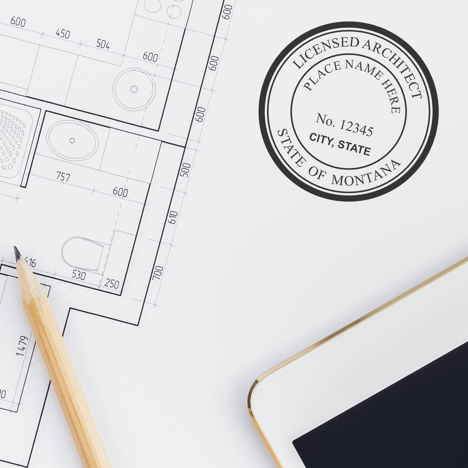 Self Inking Montana Architect Stamp in use on architectural plans, with a pencil and tablet nearby.