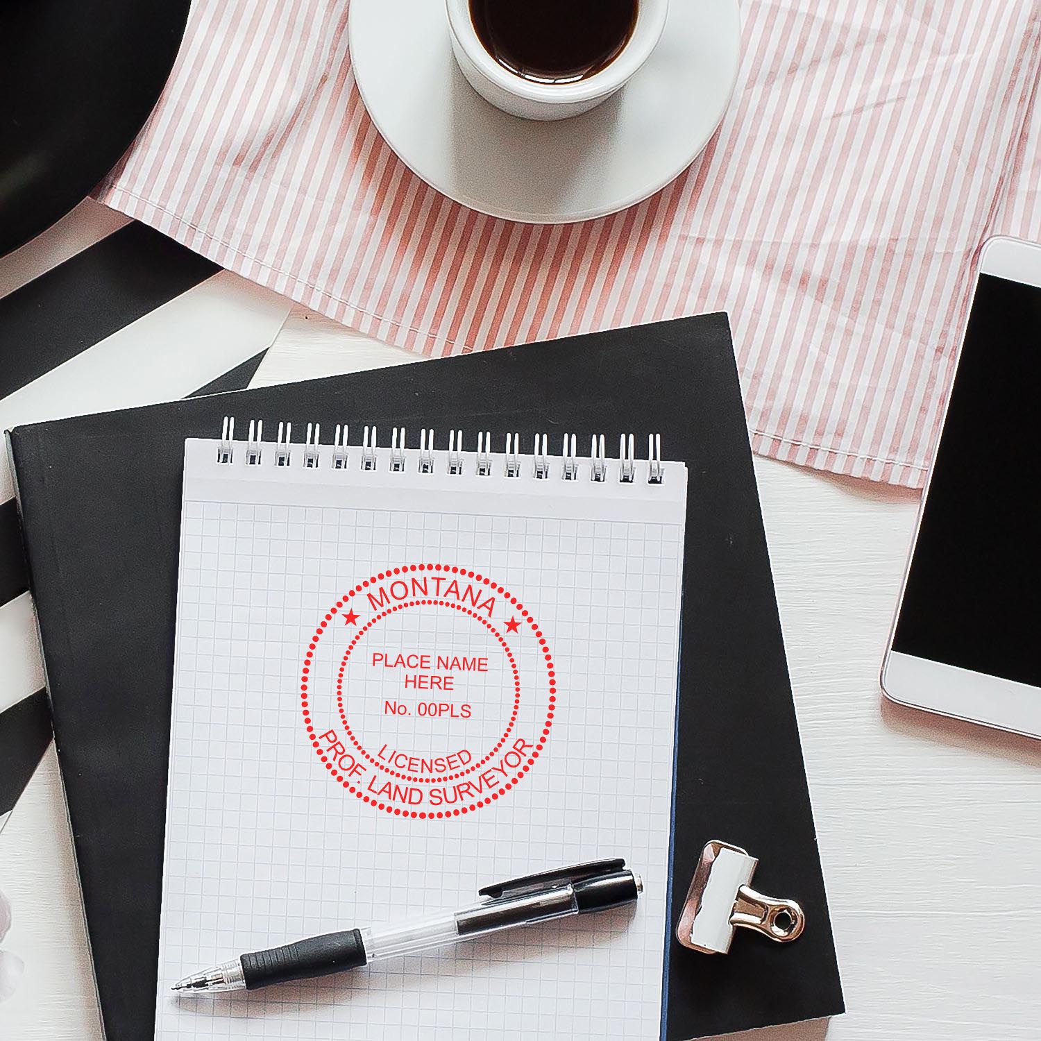 Montana Land Surveyor Seal Stamp, MT PLS Stamp on a notepad with a pen, coffee cup, and smartphone on a desk.