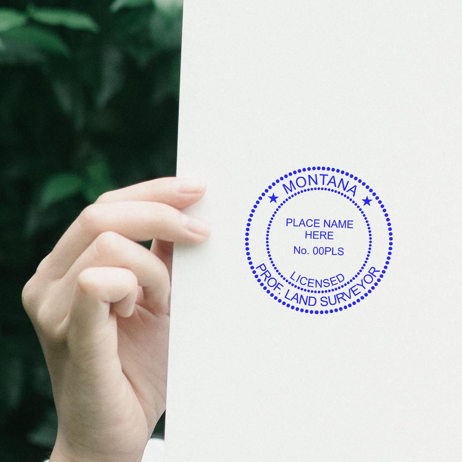 Hand holding a paper stamped with the Digital Montana Land Surveyor Stamp, Electronic Seal for Montana Land Surveyor, in blue ink.