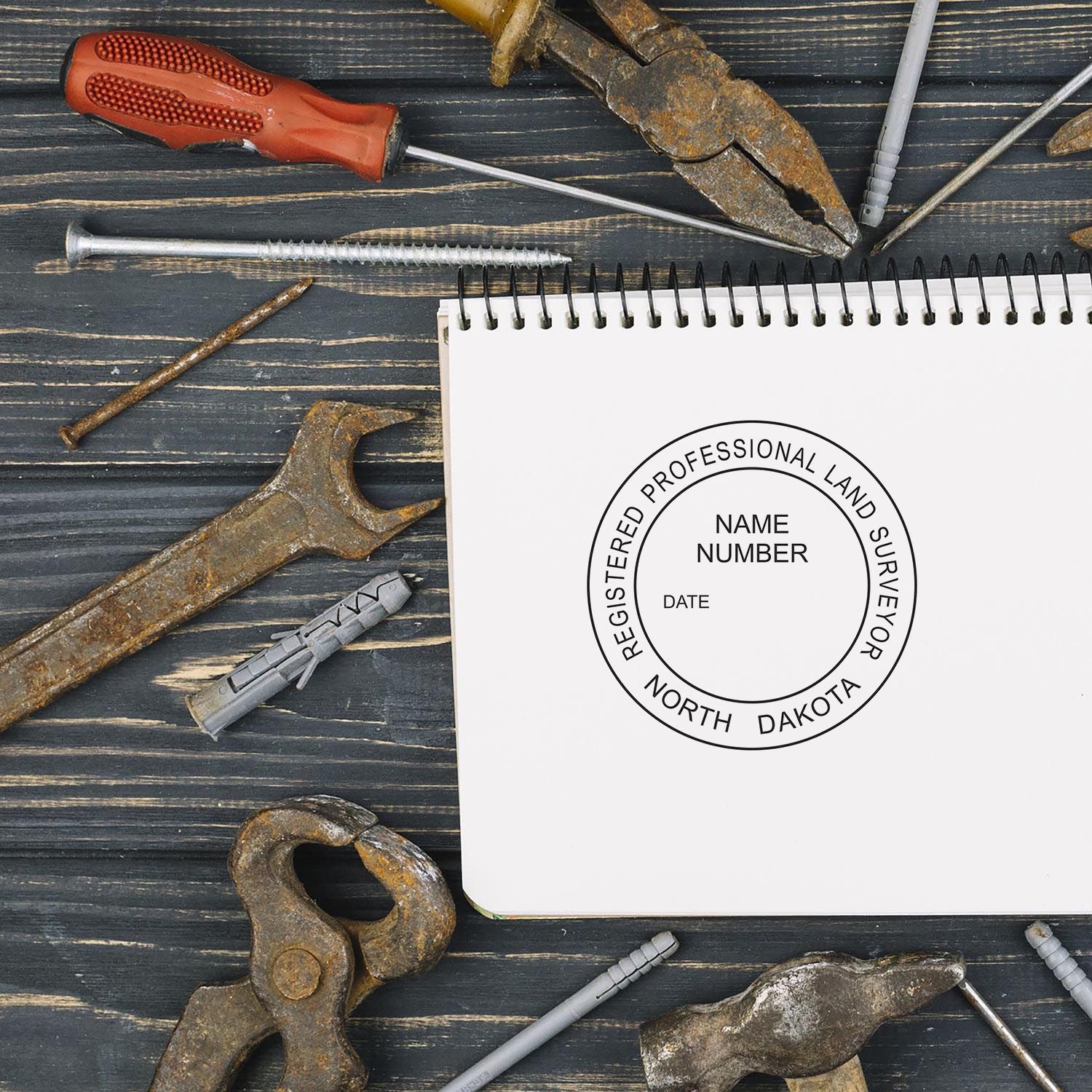 Self Inking North Dakota Land Surveyor Stamp imprint on a notebook, surrounded by various tools on a wooden surface.