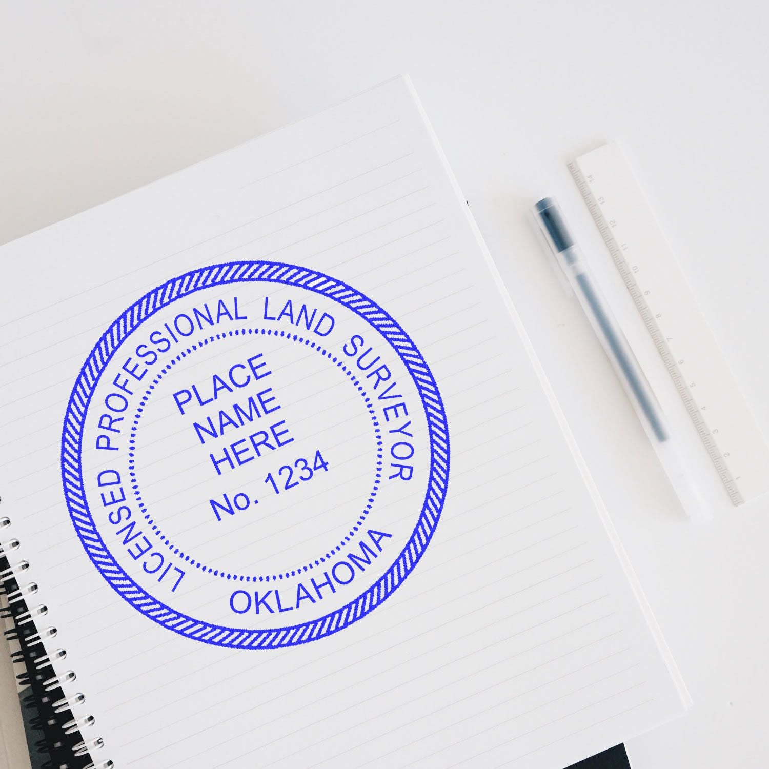 Oklahoma Land Surveyor Seal Stamp on a notebook with a pen and ruler beside it. The stamp reads "Licensed Professional Land Surveyor, Oklahoma."