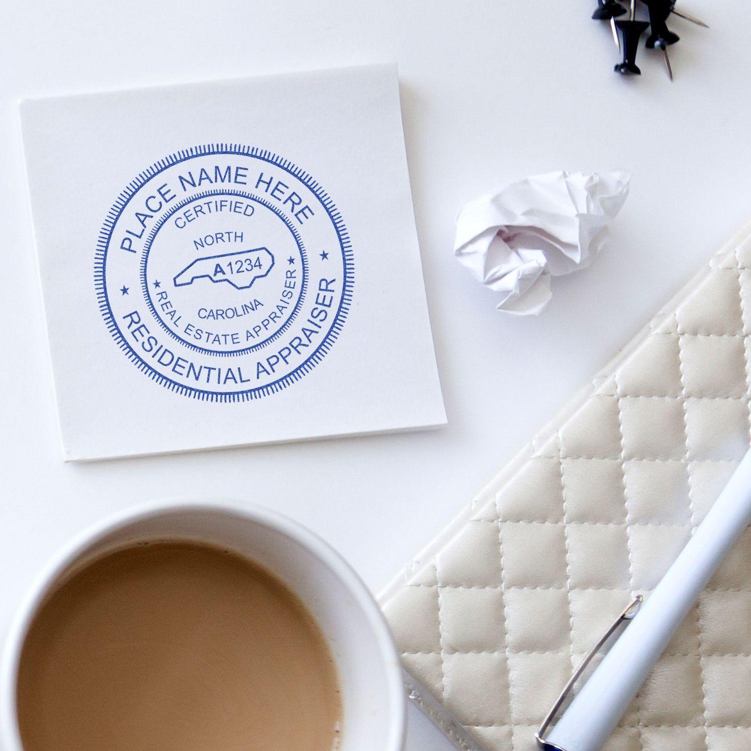 Real Estate Appraiser Regular Rubber Stamp of Seal on paper, next to a coffee cup, crumpled paper, pen, and push pins on a white desk.