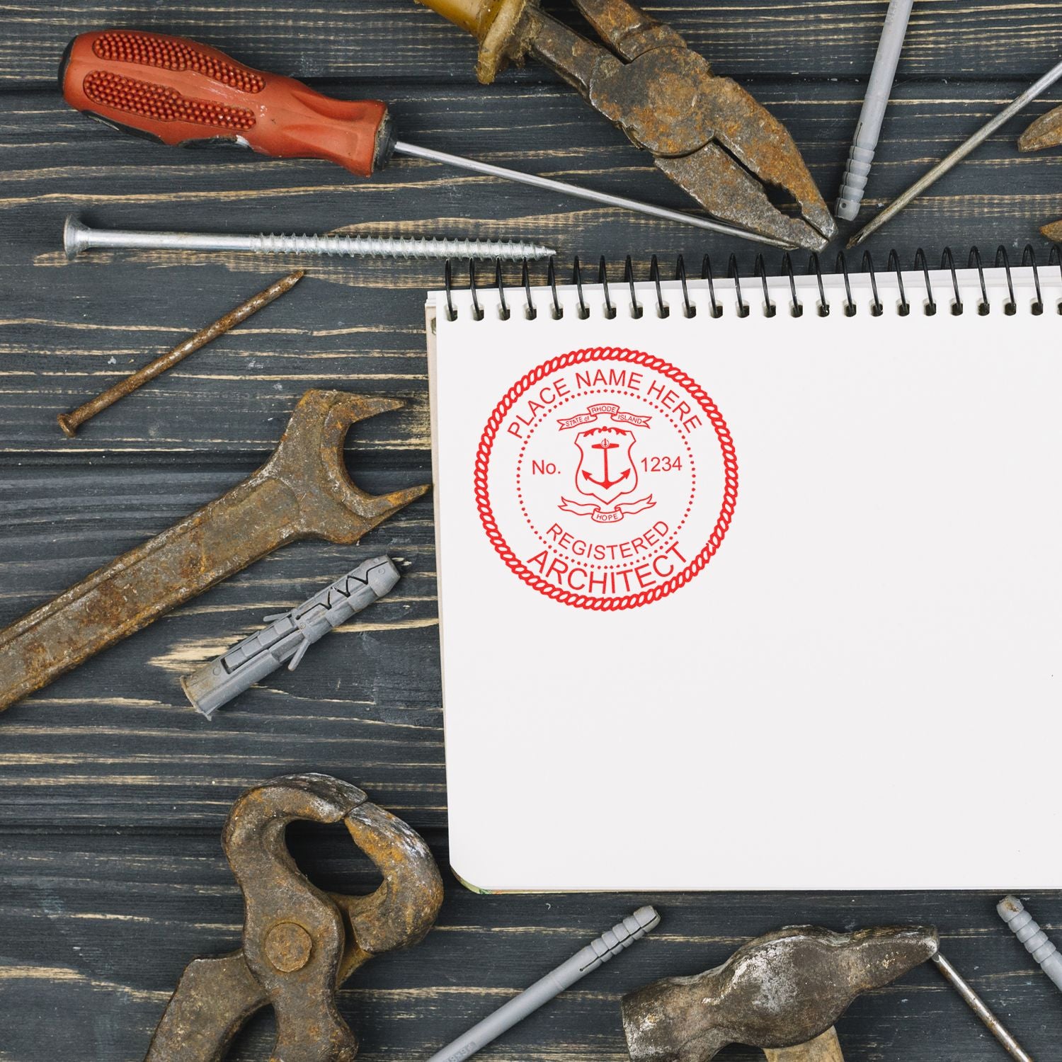 Rhode Island Architect Seal Stamp on a blank notebook surrounded by various rusty tools on a wooden surface.