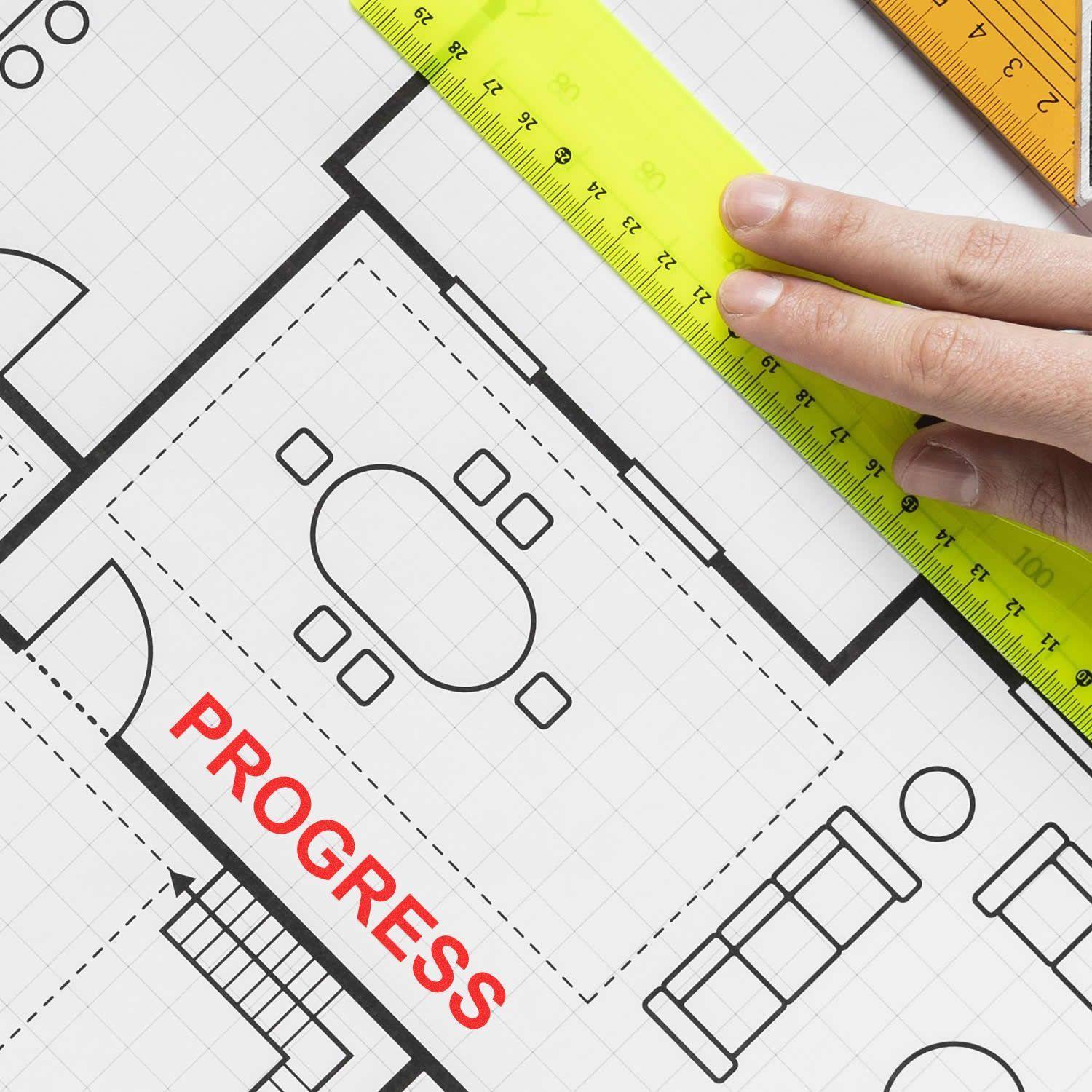 Hand holding a ruler over a floor plan with a red PROGRESS mark from a Self Inking Progress Stamp.