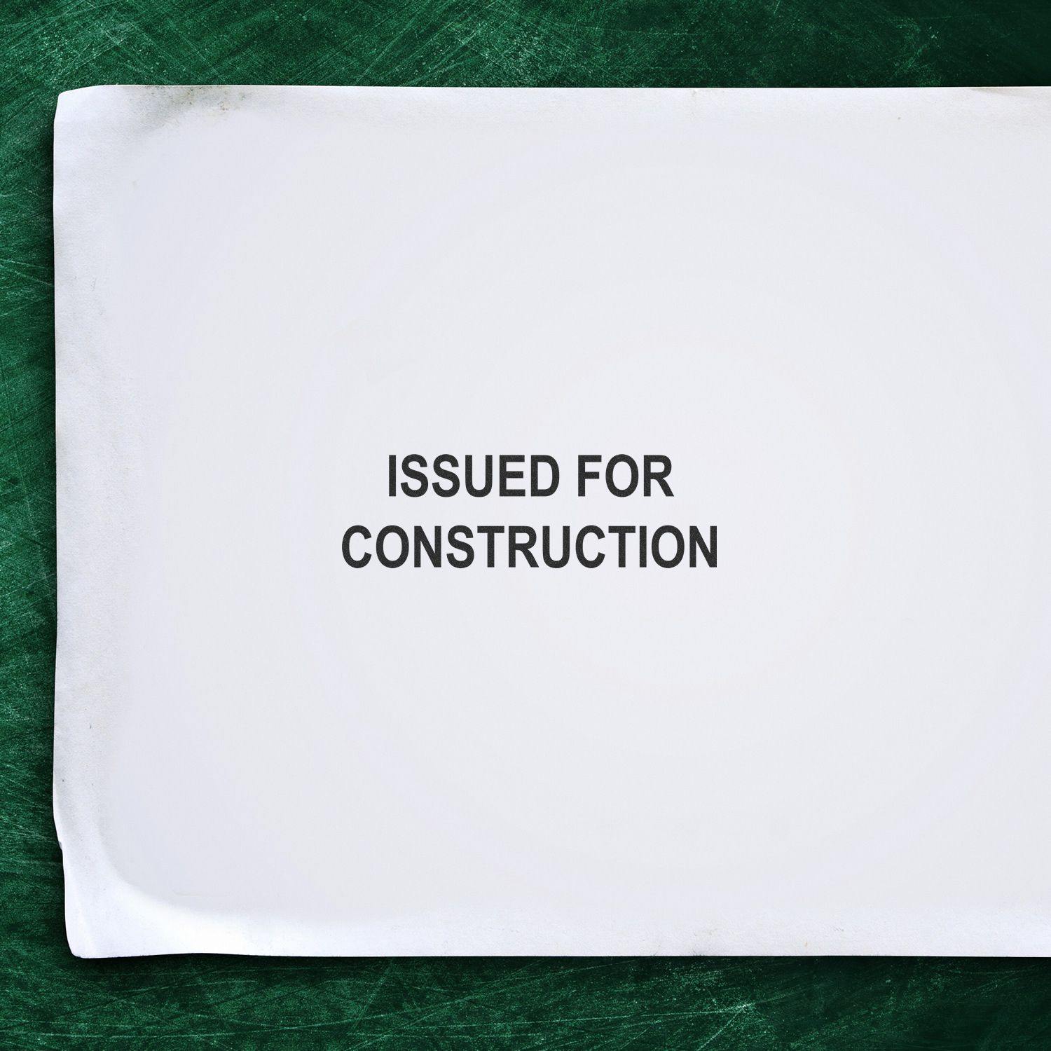 Slim Pre-Inked Issued for Construction Stamp on white paper against a green background.