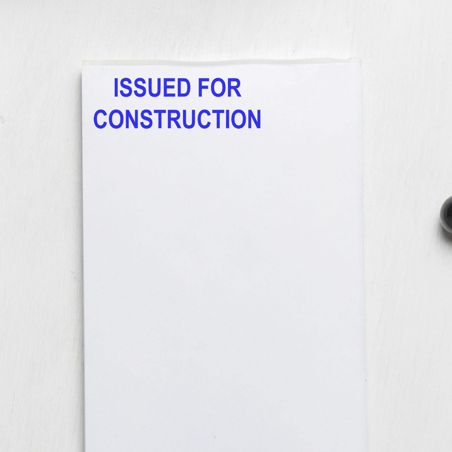 Slim Pre-Inked Issued for Construction Stamp marking a white sheet with blue text on a light background.