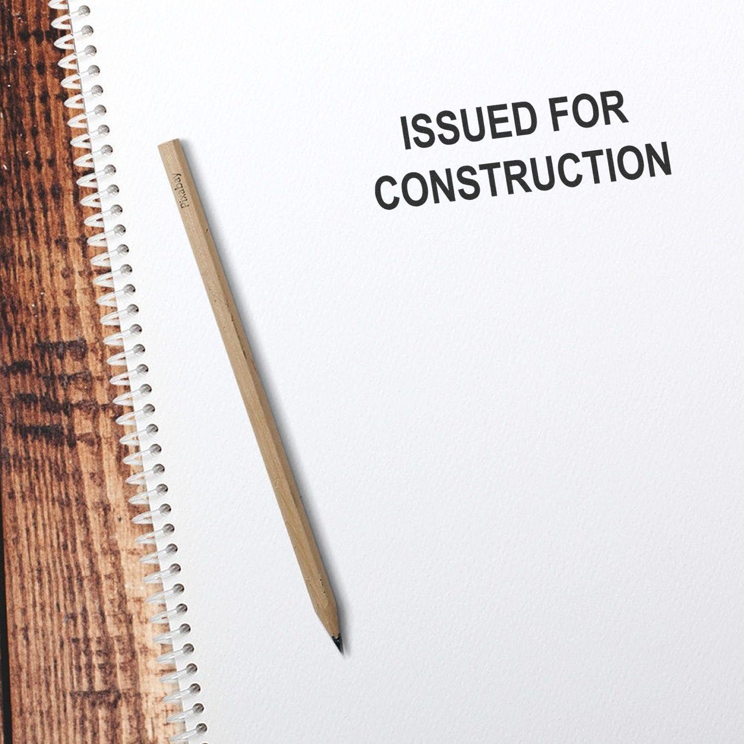 Slim Pre-Inked Issued for Construction Stamp on white paper next to a pencil on a wooden surface.