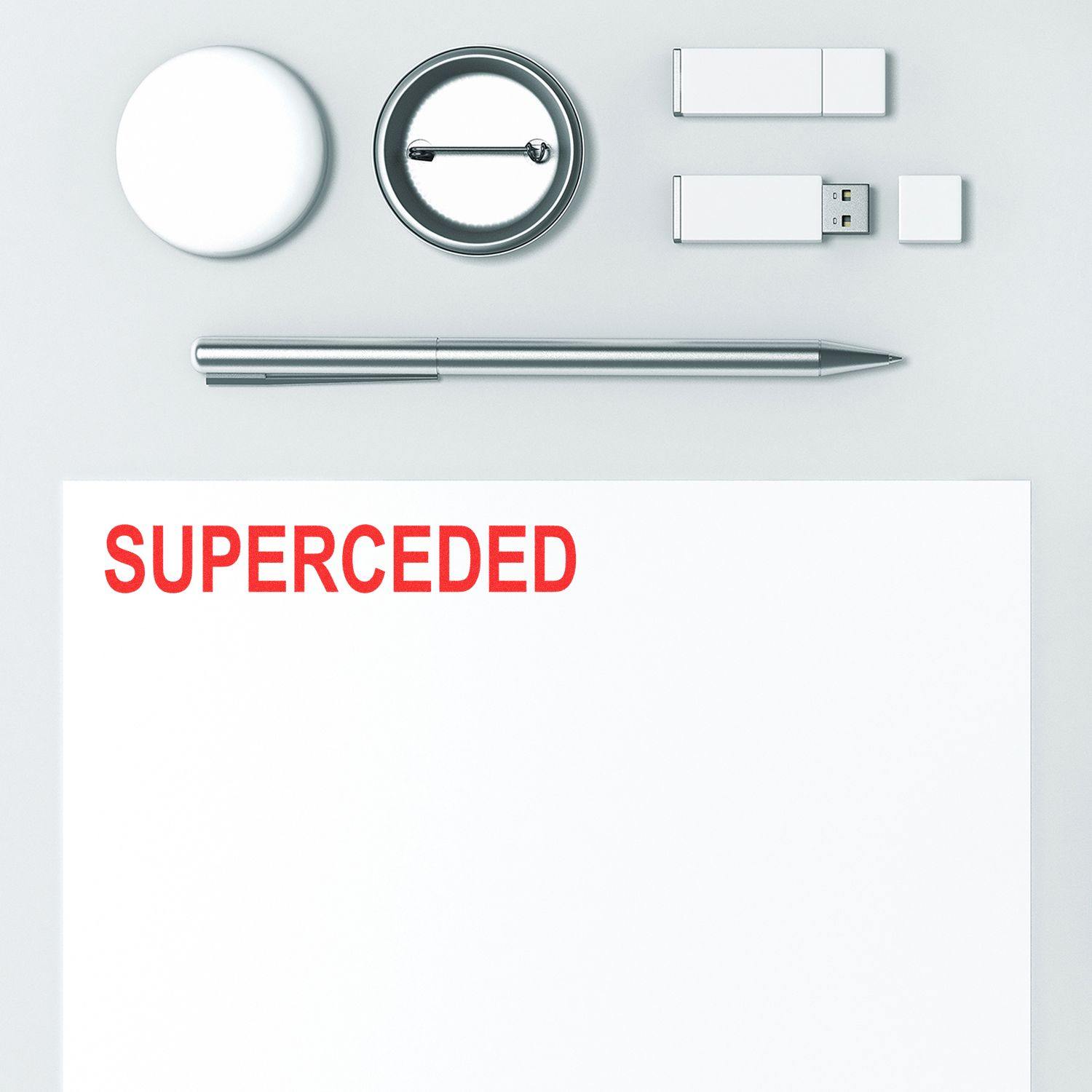 Slim Pre-Inked Superceded Stamp in use, marking SUPERCEDED in red on white paper, surrounded by office supplies.