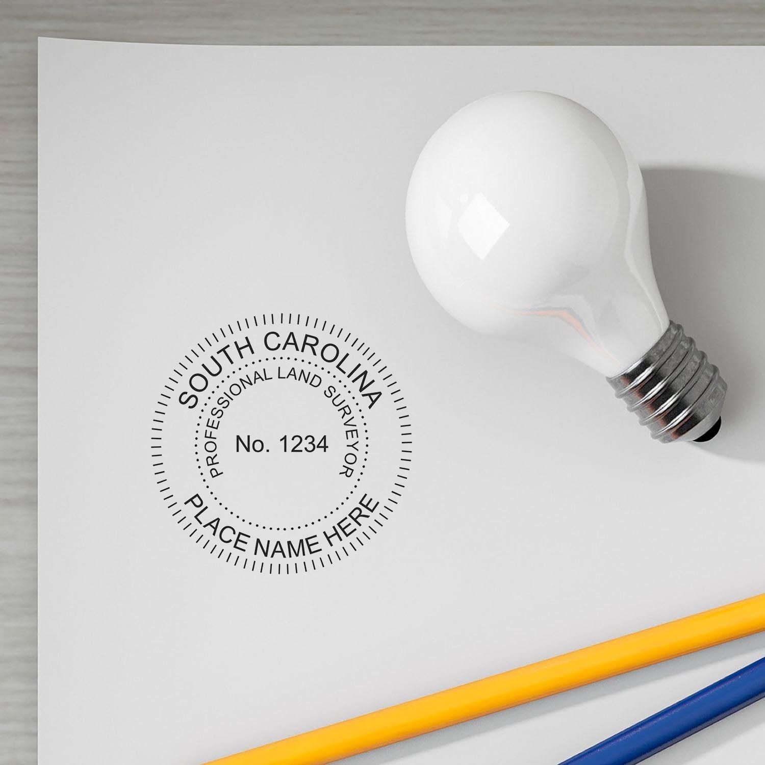 Premium MaxLight Pre-Inked South Carolina Surveyors Stamp on paper with a light bulb and pencils nearby.