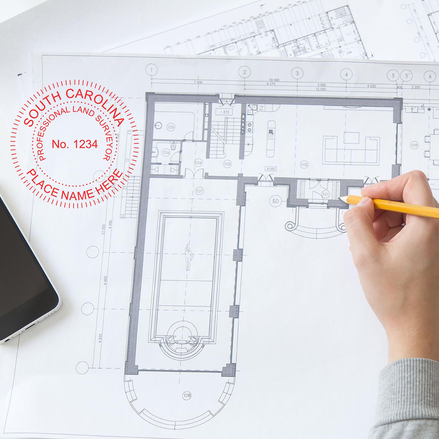 Person using South Carolina Land Surveyor Seal Stamp, SC PLS Stamp on architectural blueprints with a pencil and smartphone nearby.