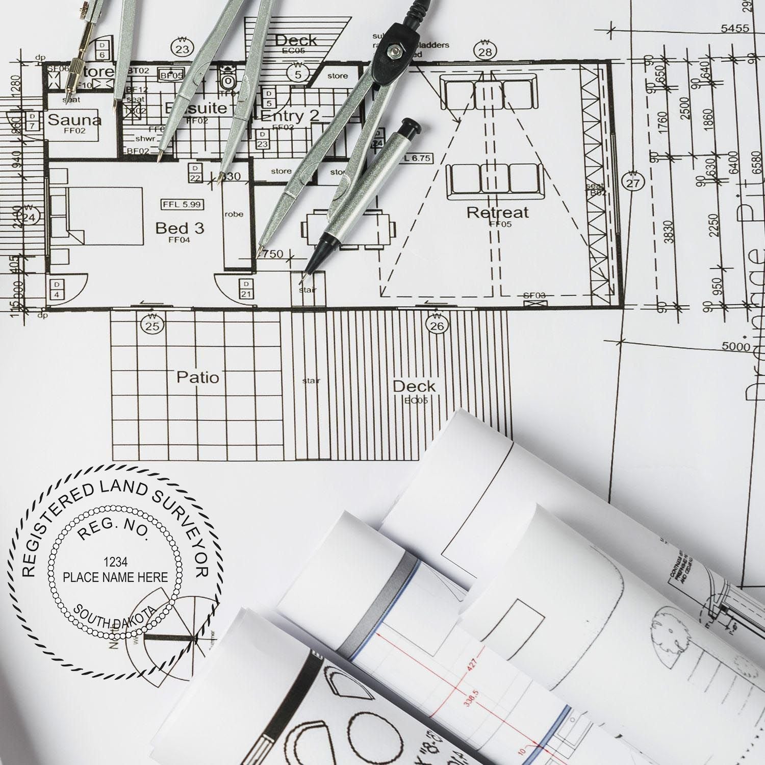 Blueprints with a Premium MaxLight Pre-Inked South Dakota Surveyors Stamp, compass, and rolled architectural plans on a desk.