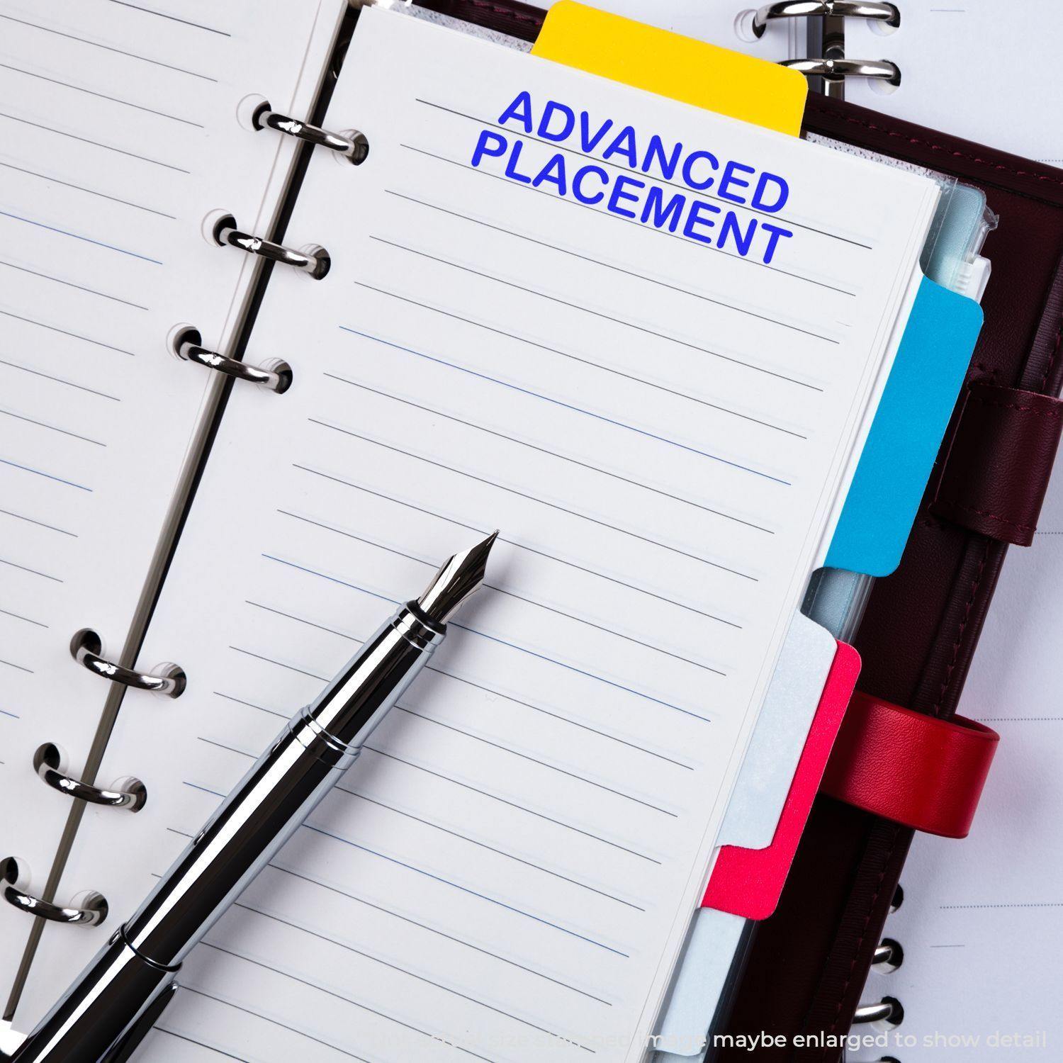 A planner with a Large Advanced Placement Rubber Stamp mark on a page, next to a fountain pen and colorful tab dividers.