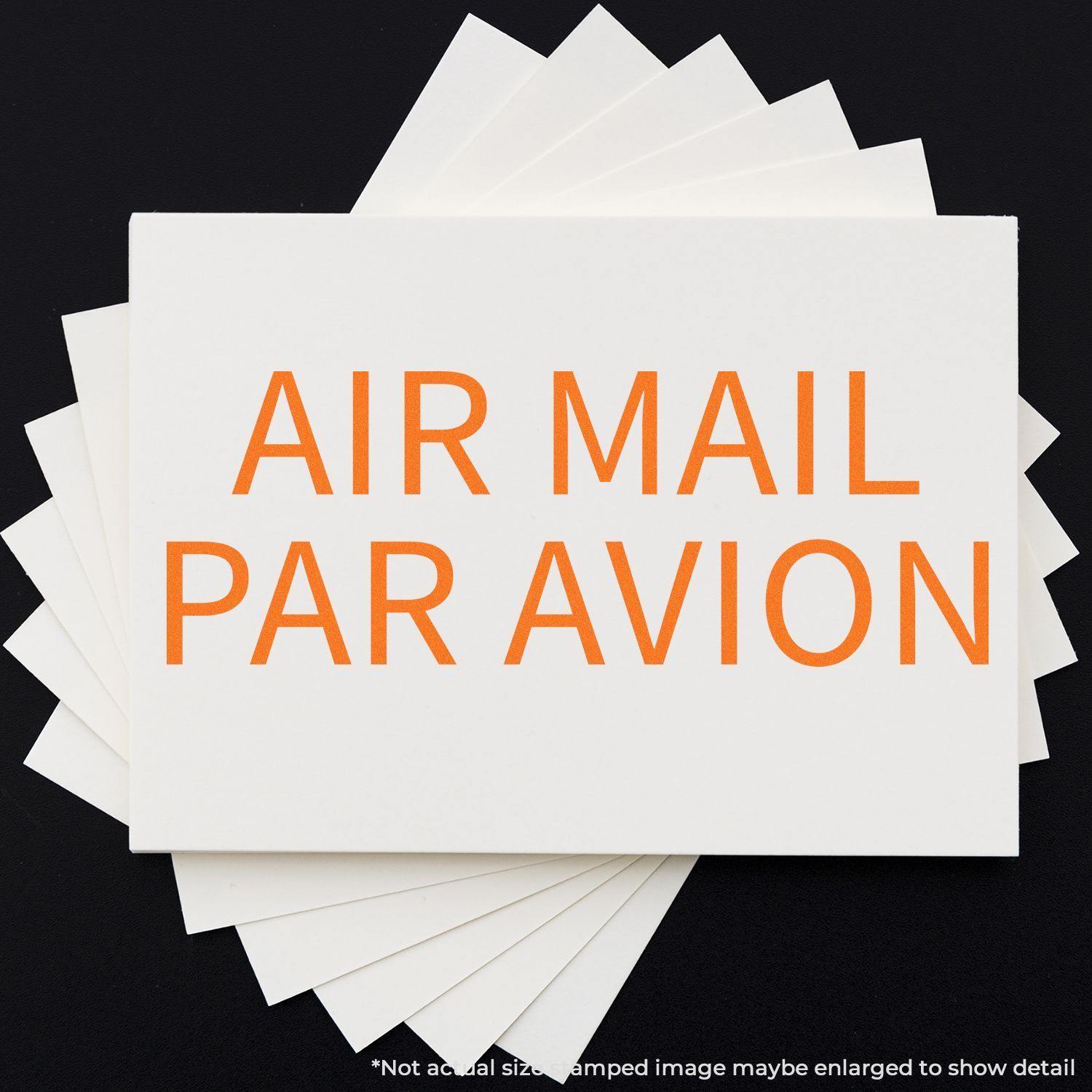 Large Air Mail Par Avion Rubber Stamp in use, displaying bold orange text on white paper, with multiple sheets fanned out underneath.