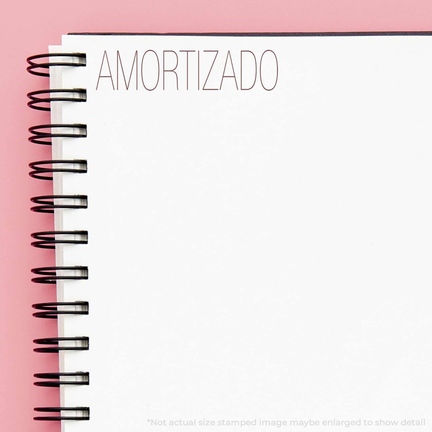 Self Inking Amortizado Stamp imprint on a white spiral notebook page with a pink background.