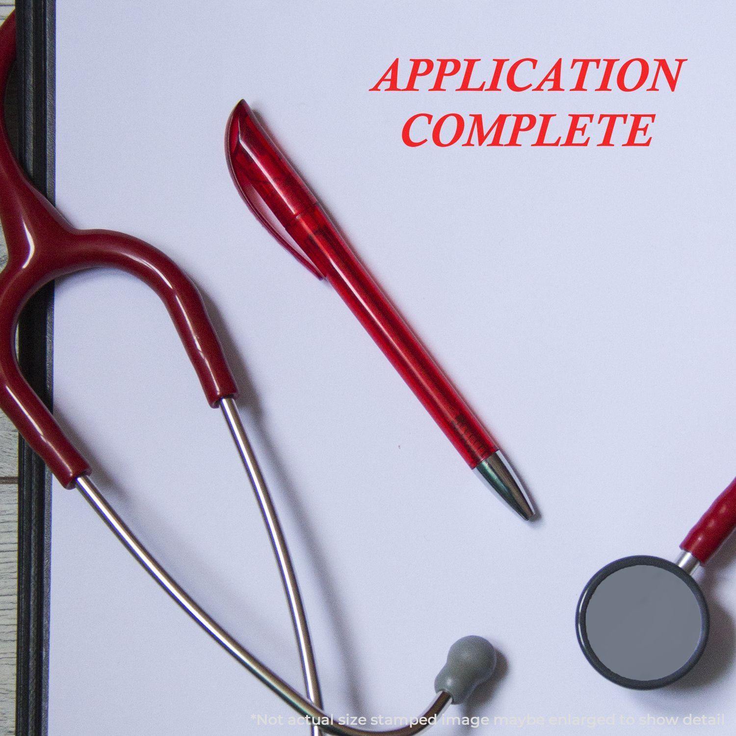 A Large Application Complete Rubber Stamp is used on a white paper, surrounded by a red pen and a stethoscope.