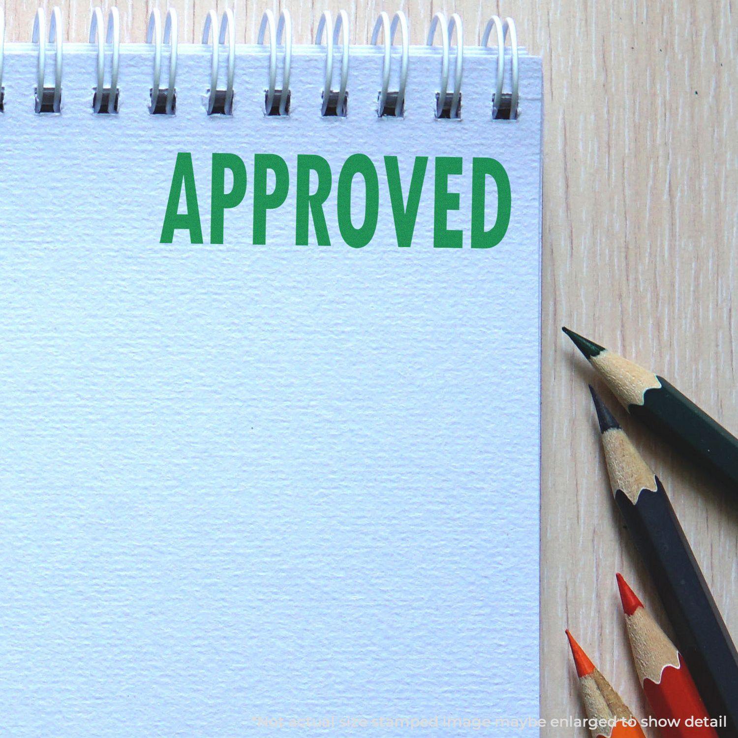 A notepad with "APPROVED" stamped in green using an Approved Rubber Stamp, next to colored pencils on a wooden surface.