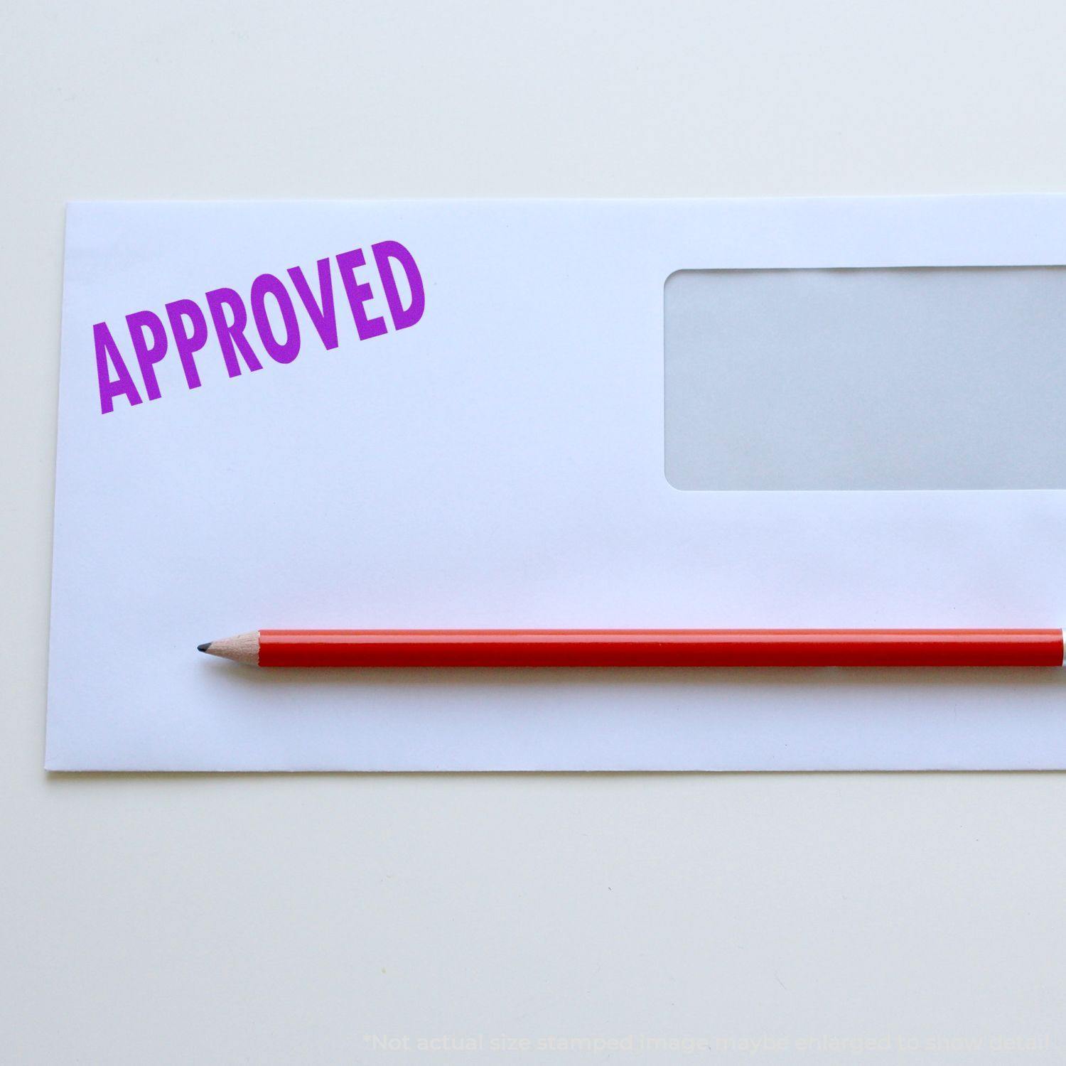 Envelope with an 'Approved' rubber stamp in purple ink and a red pencil placed on a white surface.