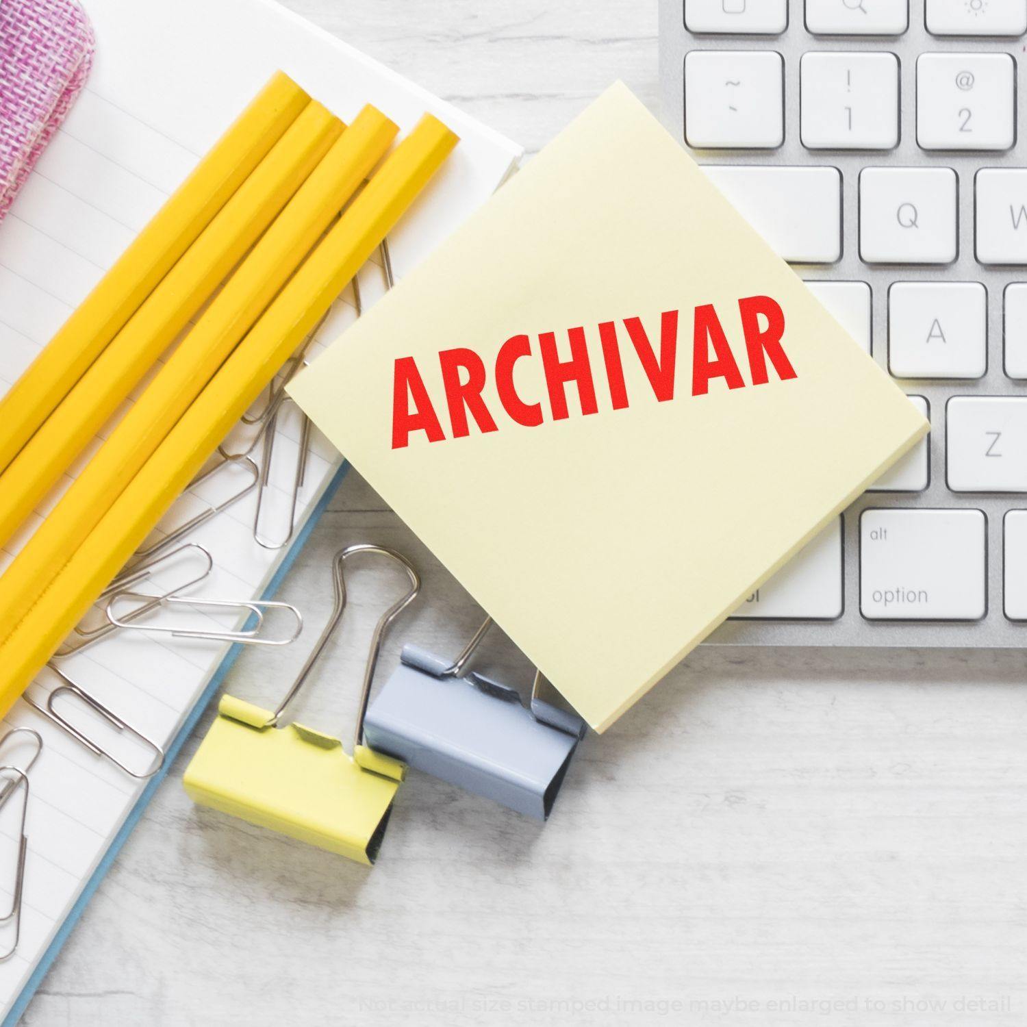 Self Inking Archivar Stamp on a sticky note beside a keyboard, pencils, paper clips, and binder clips on a desk.