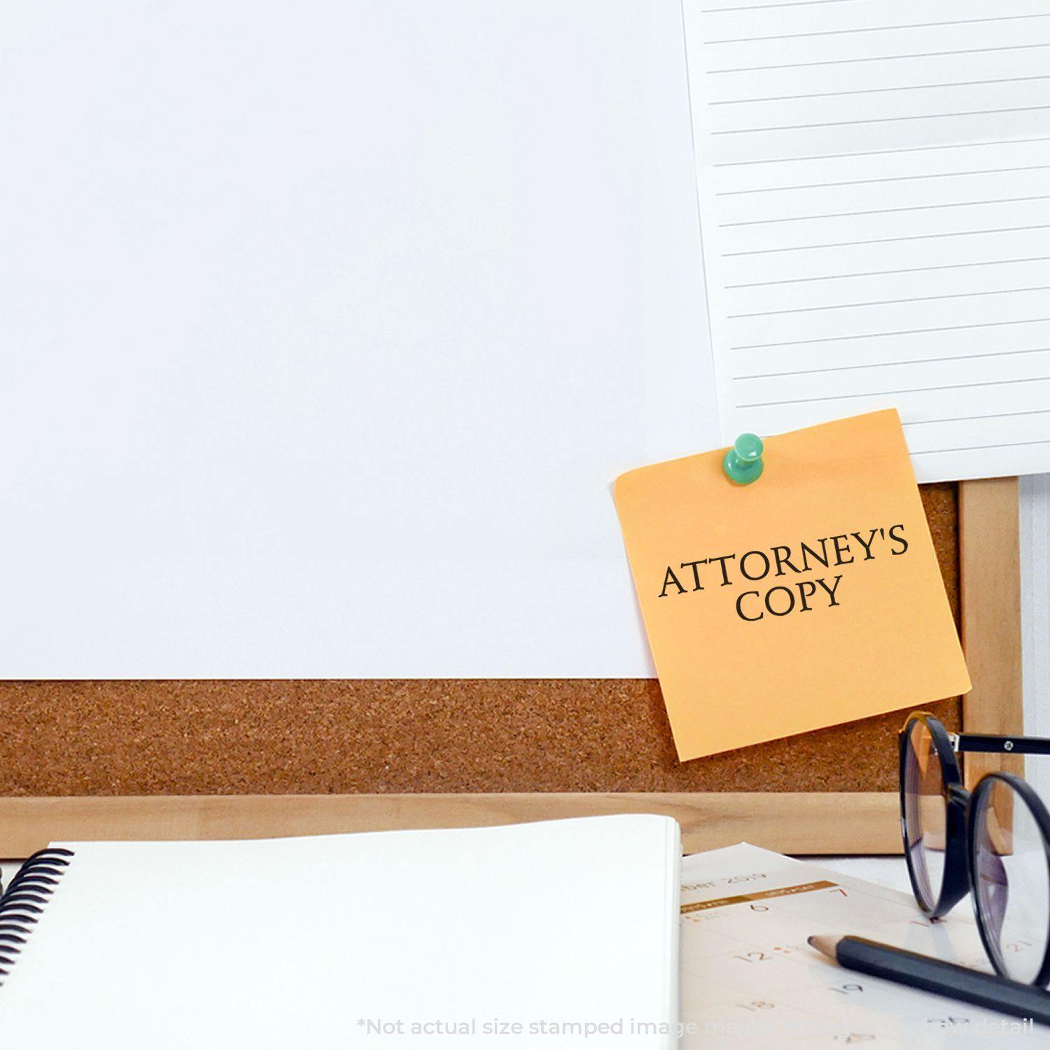 Large Attorneys Copy Rubber Stamp used on a yellow sticky note pinned to a corkboard, with office supplies like a notebook and glasses nearby.