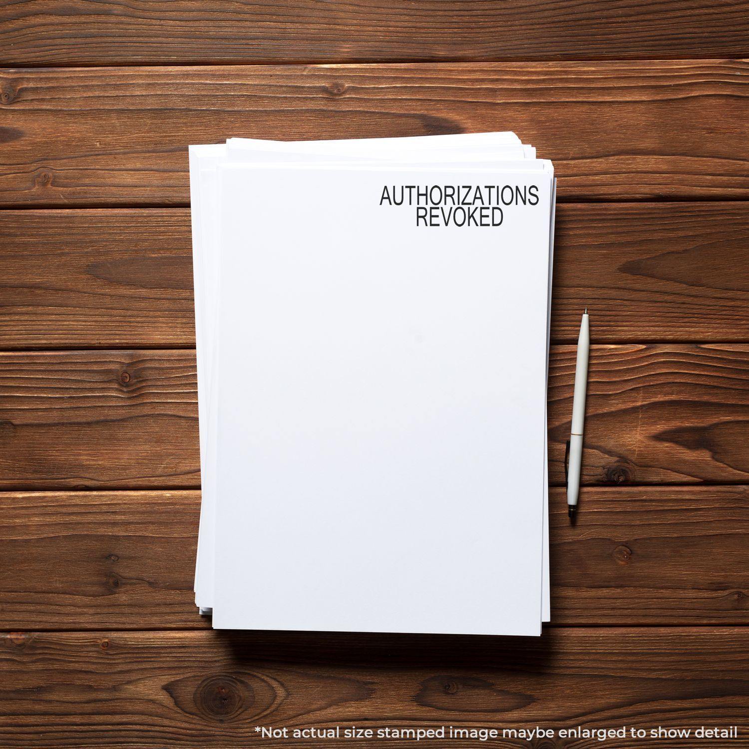 A stack of papers stamped with AUTHORIZATIONS REVOKED using the Large Authorizations Revoked Rubber Stamp, placed on a wooden desk with a pen.