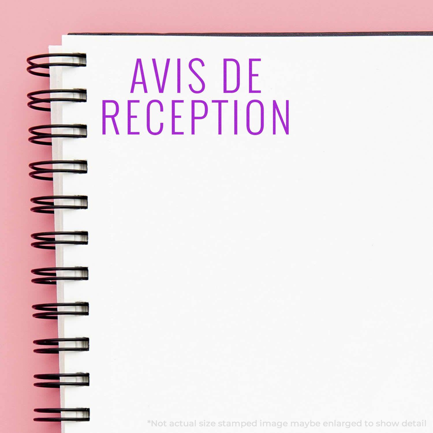 Self Inking Avis De Reception Stamp on a white spiral notebook with a pink background.