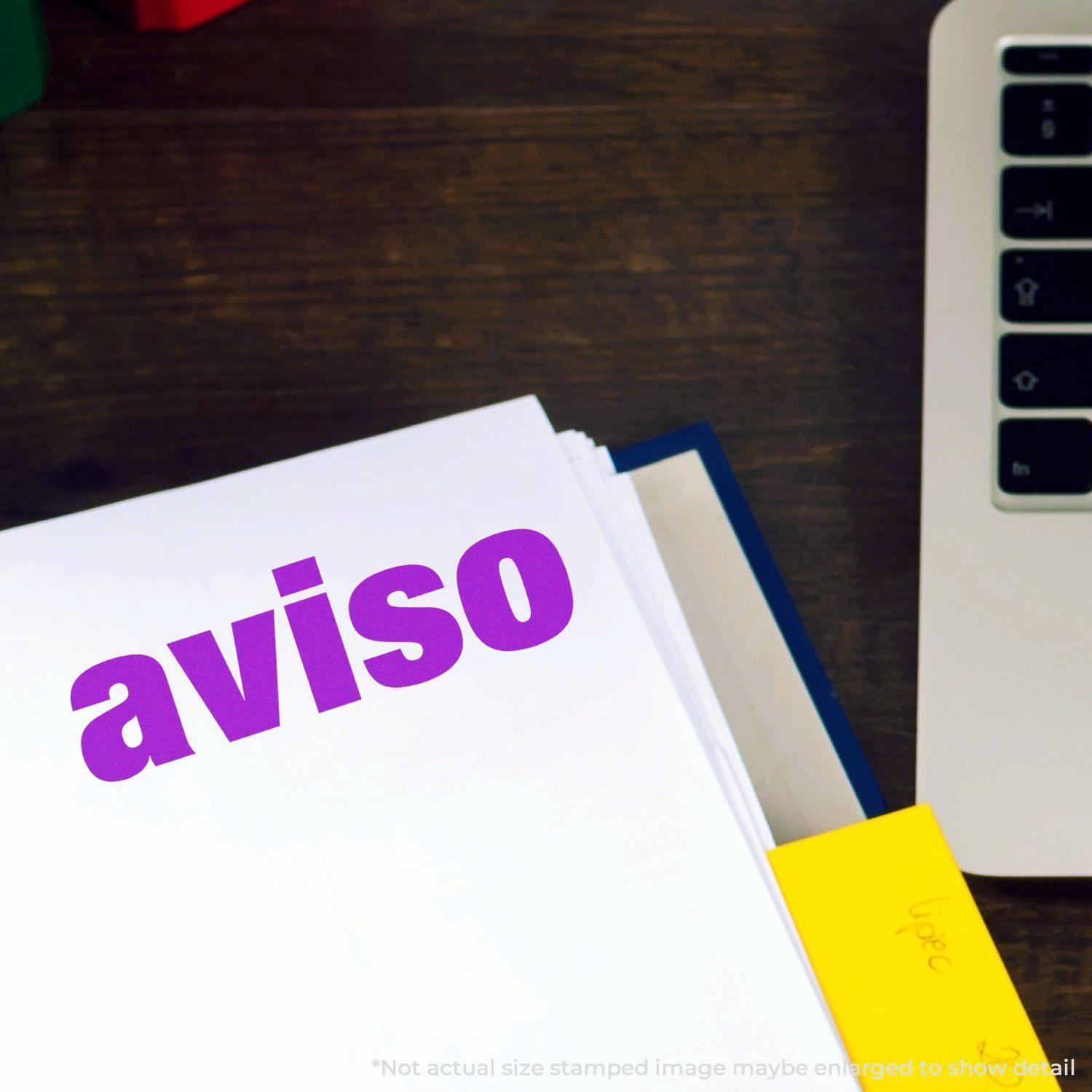 Large Aviso Rubber Stamp in purple ink on white paper, next to a laptop and yellow sticky note on a wooden desk.