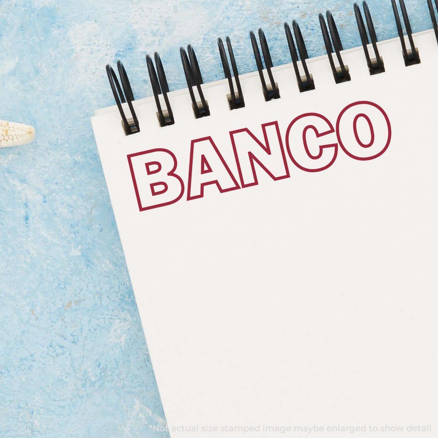 A Self Inking Banco Stamp imprint on a white notepad with a blue textured background.