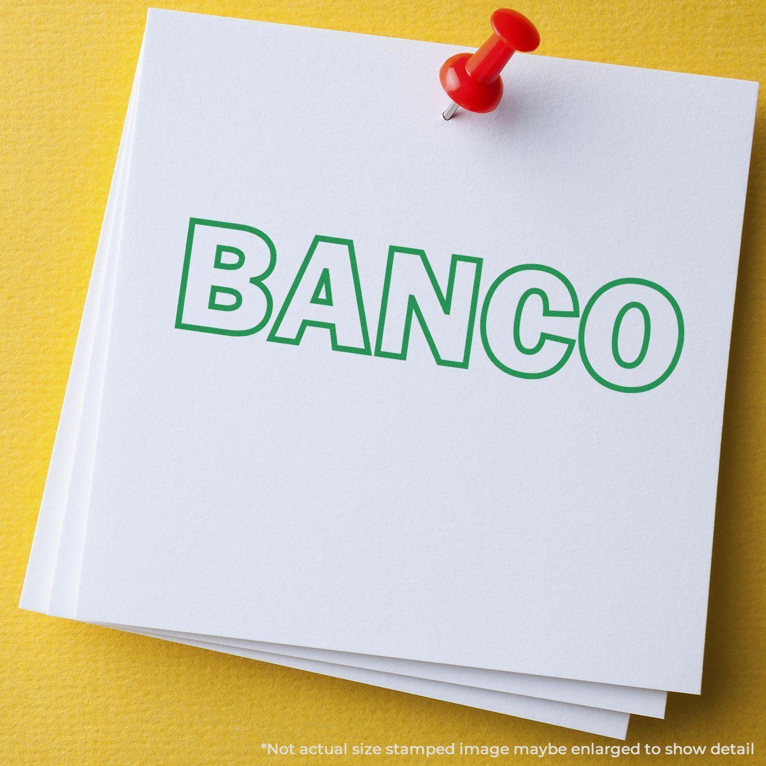 White paper with BANCO stamped in green ink using a Banco Rubber Stamp, pinned with a red pushpin on a yellow surface.