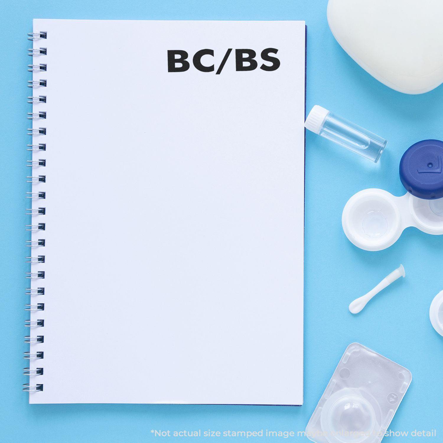 A Self Inking BC/BS Stamp is used on a white spiral notebook, surrounded by medical supplies on a blue background.