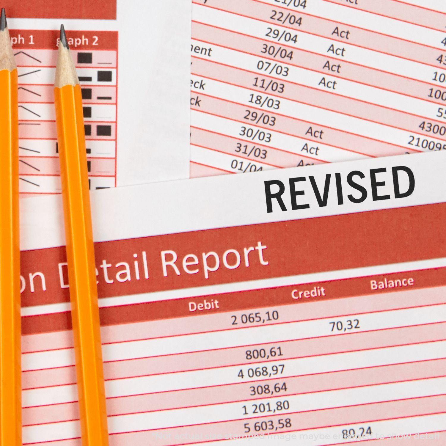 Two pencils on a financial report stamped with REVISED using a Slim Pre-Inked Revised Stamp, highlighting updated data.