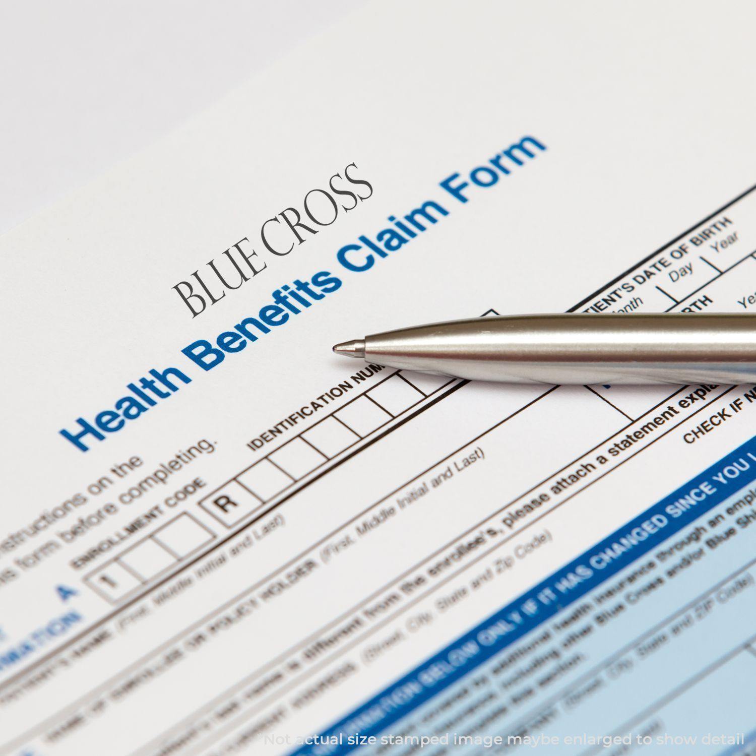 A Large Pre-Inked Blue Cross Stamp is used on a health benefits claim form, with a pen placed nearby for filling out details.