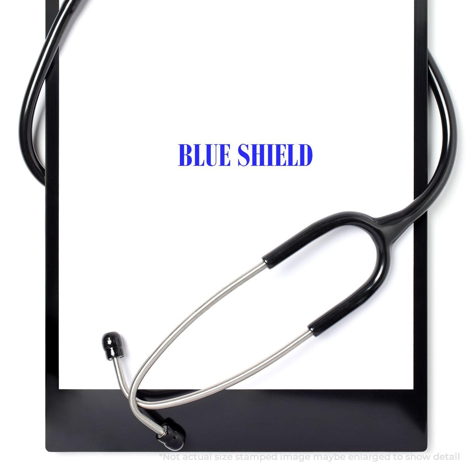 A stethoscope rests on a clipboard with a paper stamped BLUE SHIELD using the Large Blue Shield Rubber Stamp.