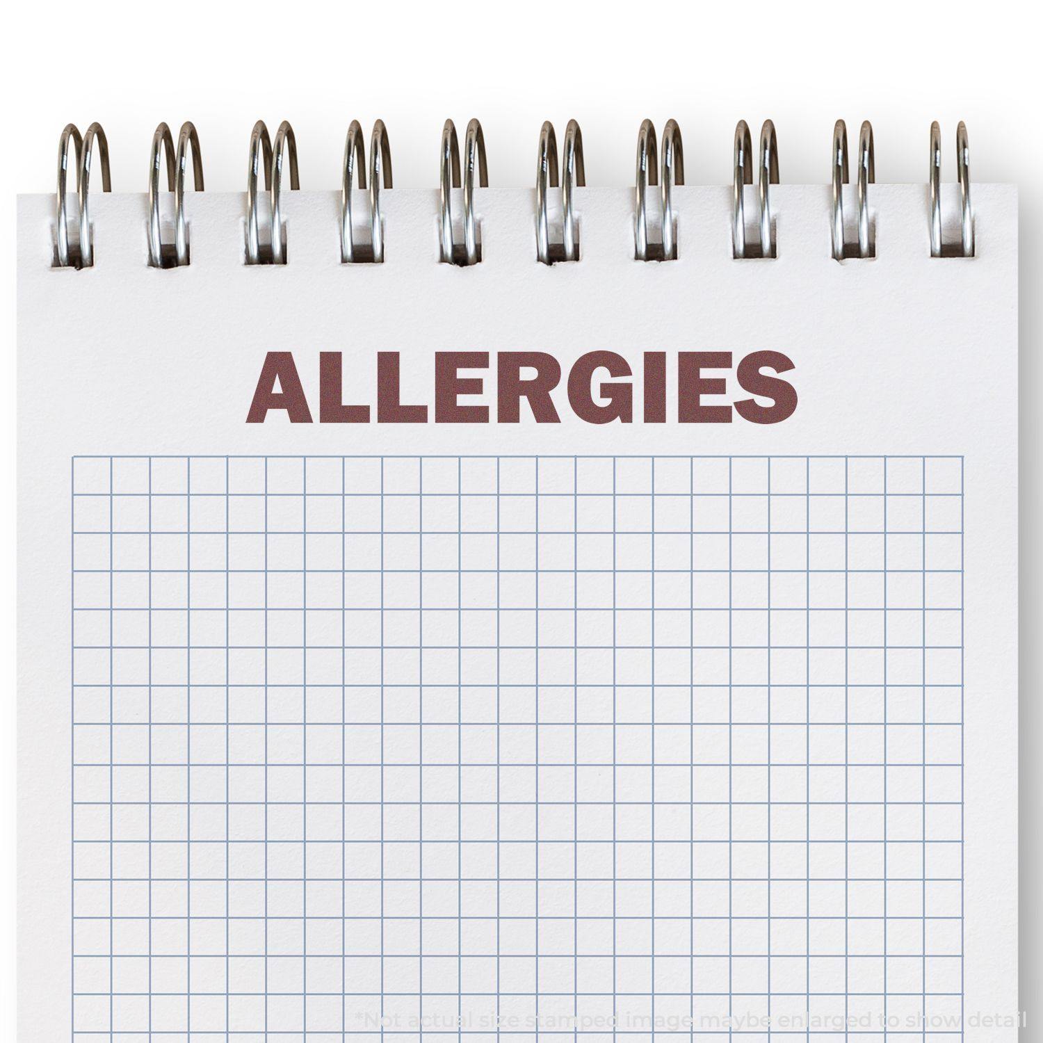 Self Inking Bold Allergies Stamp marking ALLERGIES in bold red ink on a spiral-bound notepad with a grid pattern.