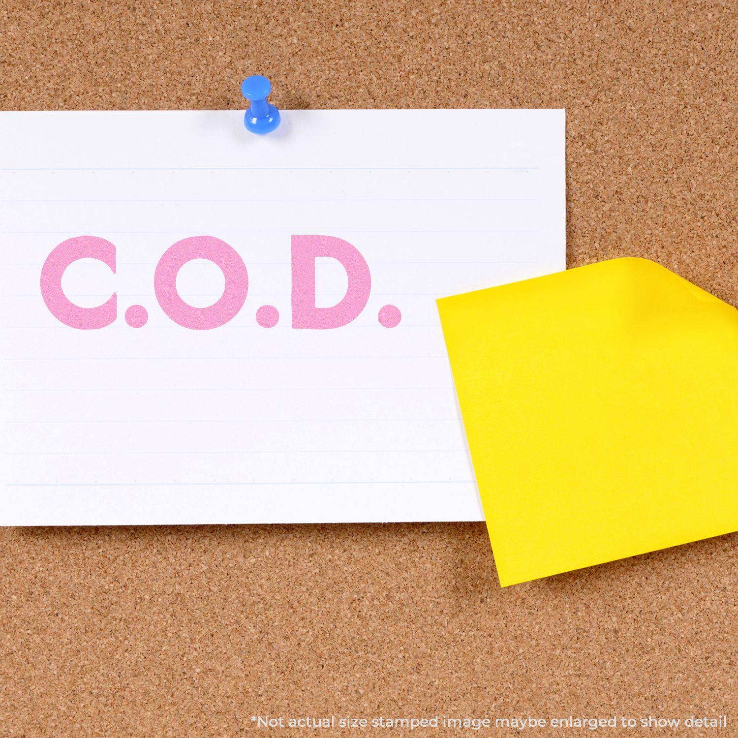 A Large Pre-Inked Bold COD Stamp imprint on a white card pinned to a corkboard, with a yellow sticky note partially covering the card.