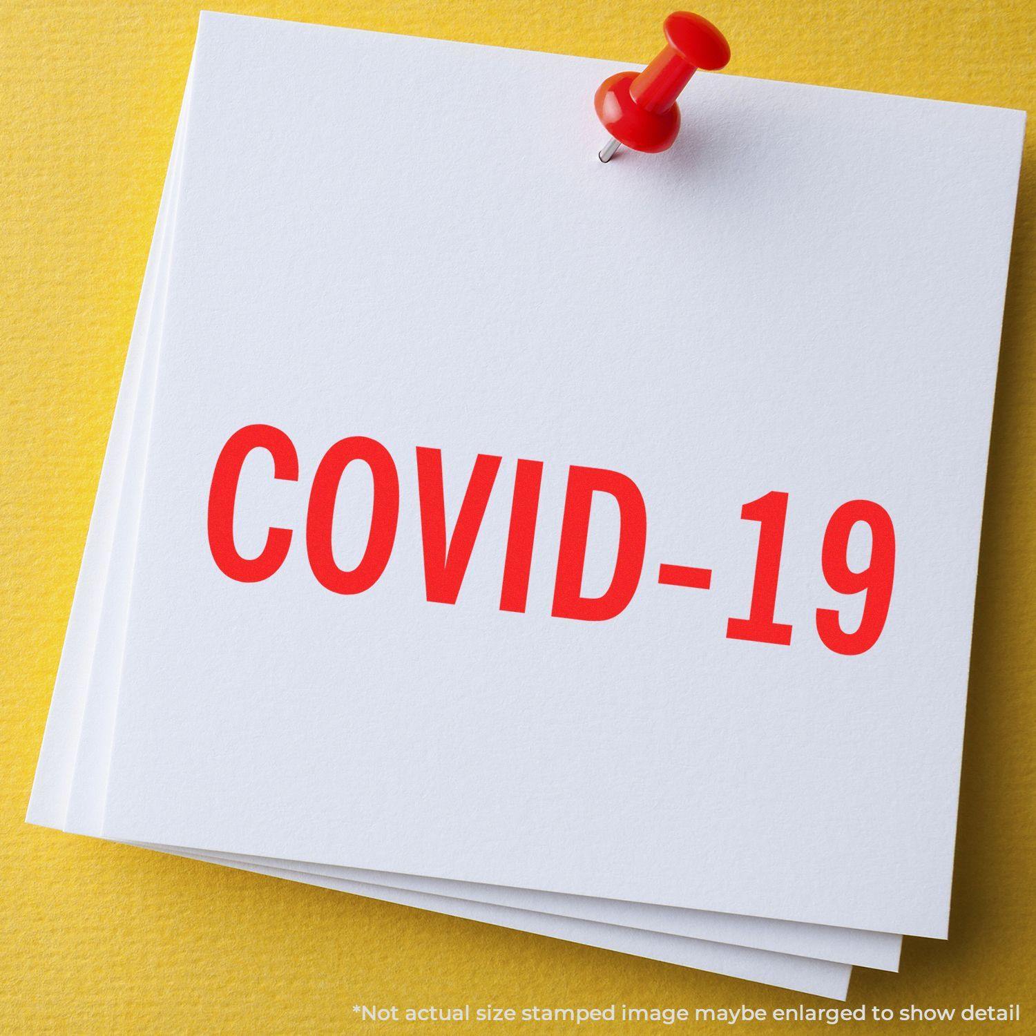 Bold Covid-19 Rubber Stamp in red ink on white paper, pinned with a red pushpin against a yellow background.