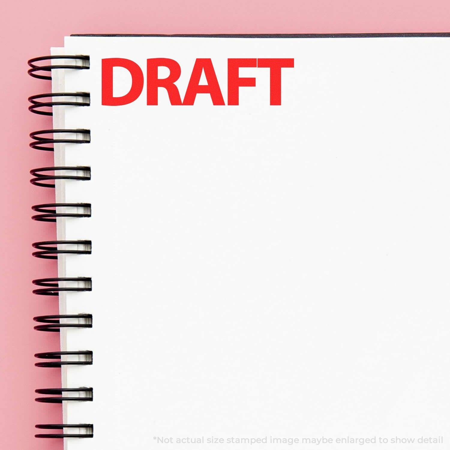 A spiral notebook with a DRAFT Bold Draft Rubber Stamp in red ink on the top left corner of the page against a pink background.