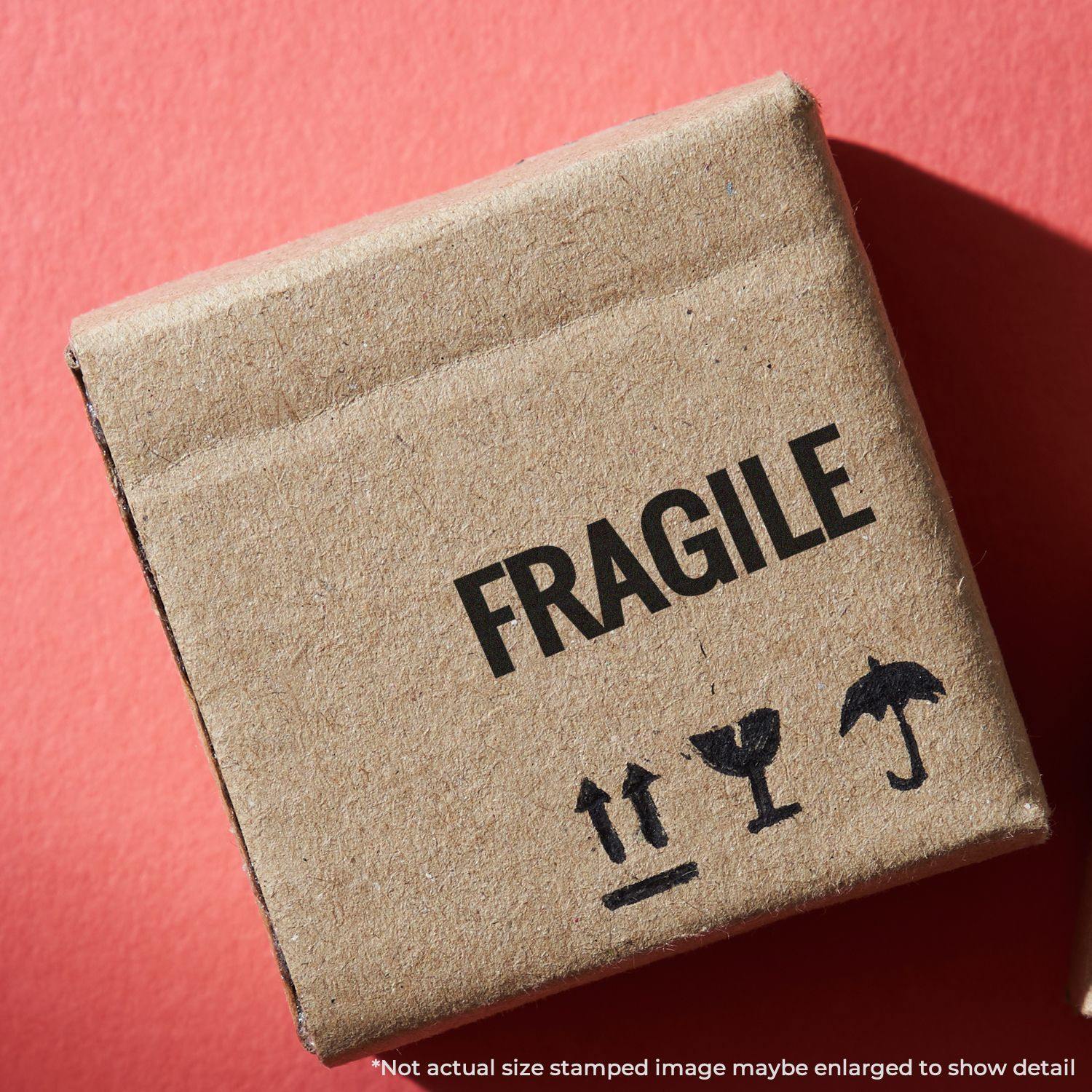 Cardboard box stamped with FRAGILE using the Large Bold Fragile Rubber Stamp, placed on a red background.