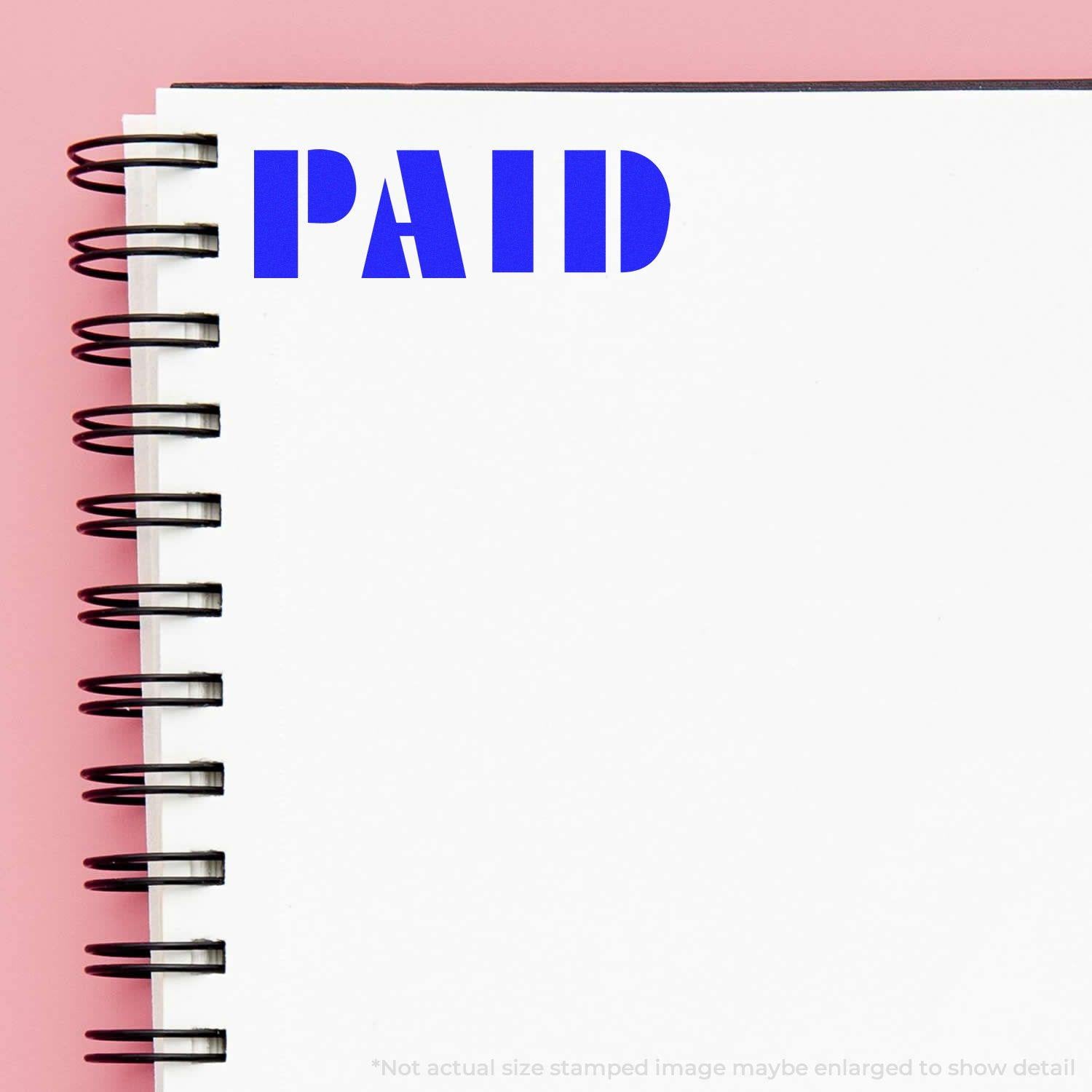 Bold Paid rubber stamp in blue ink on a white spiral notebook page with a pink background.