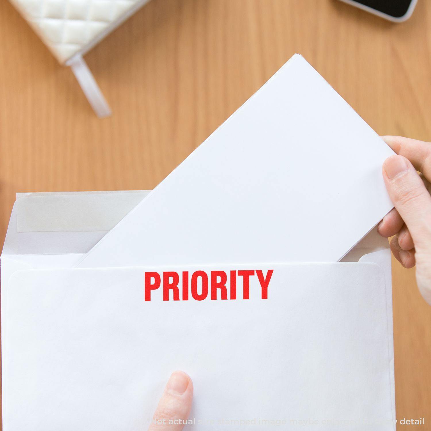 Person using Large Pre-Inked Bold Priority Stamp on a white envelope, with the word PRIORITY clearly visible in red.