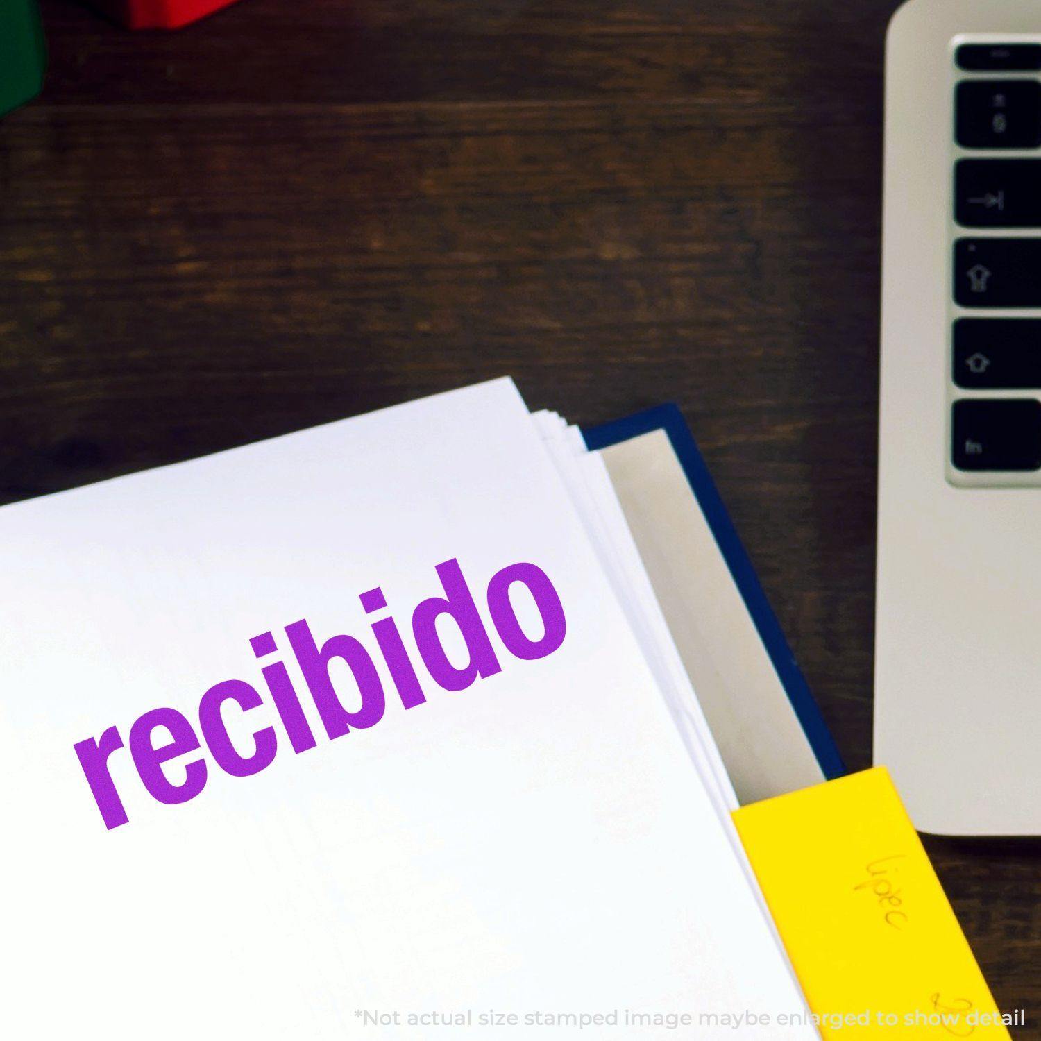 Large Pre-Inked Bold Recibido Stamp in purple ink on a white document, next to a laptop and yellow sticky notes on a wooden desk.