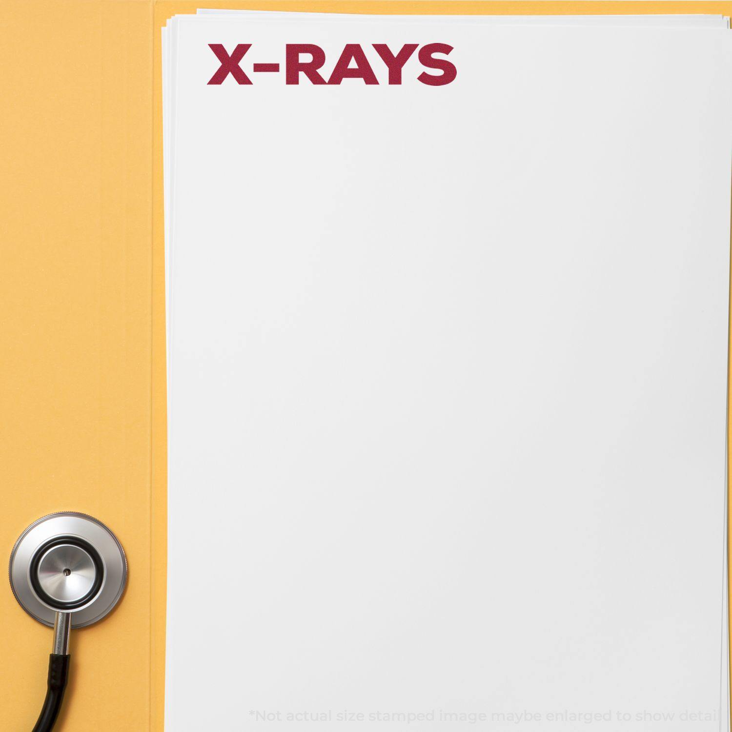 Large Self Inking Bold X-Rays Stamp marking X-RAYS in red on a stack of white papers next to a stethoscope on a yellow surface.